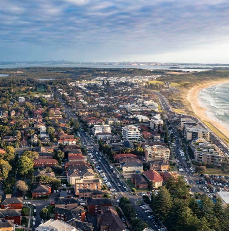 Aerial view of a coastal town featuring residential buildings, a main road, a beach, and the ocean with gentle waves; the sky is partly cloudy—reflecting an atmosphere akin to seamless process improvement.