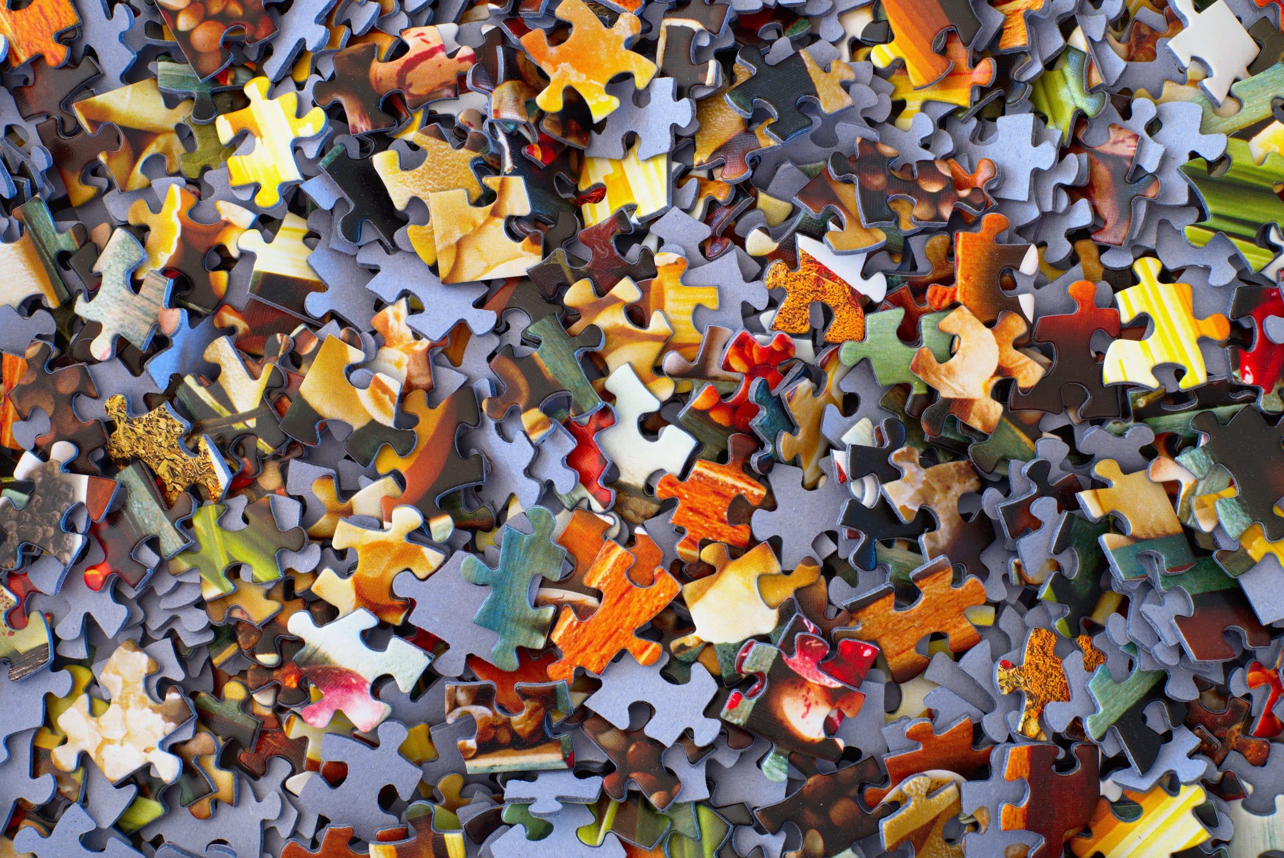 A close-up of numerous mixed jigsaw puzzle pieces, displaying various colors and patterns, scattered randomly, much like the initial stages of process improvement.