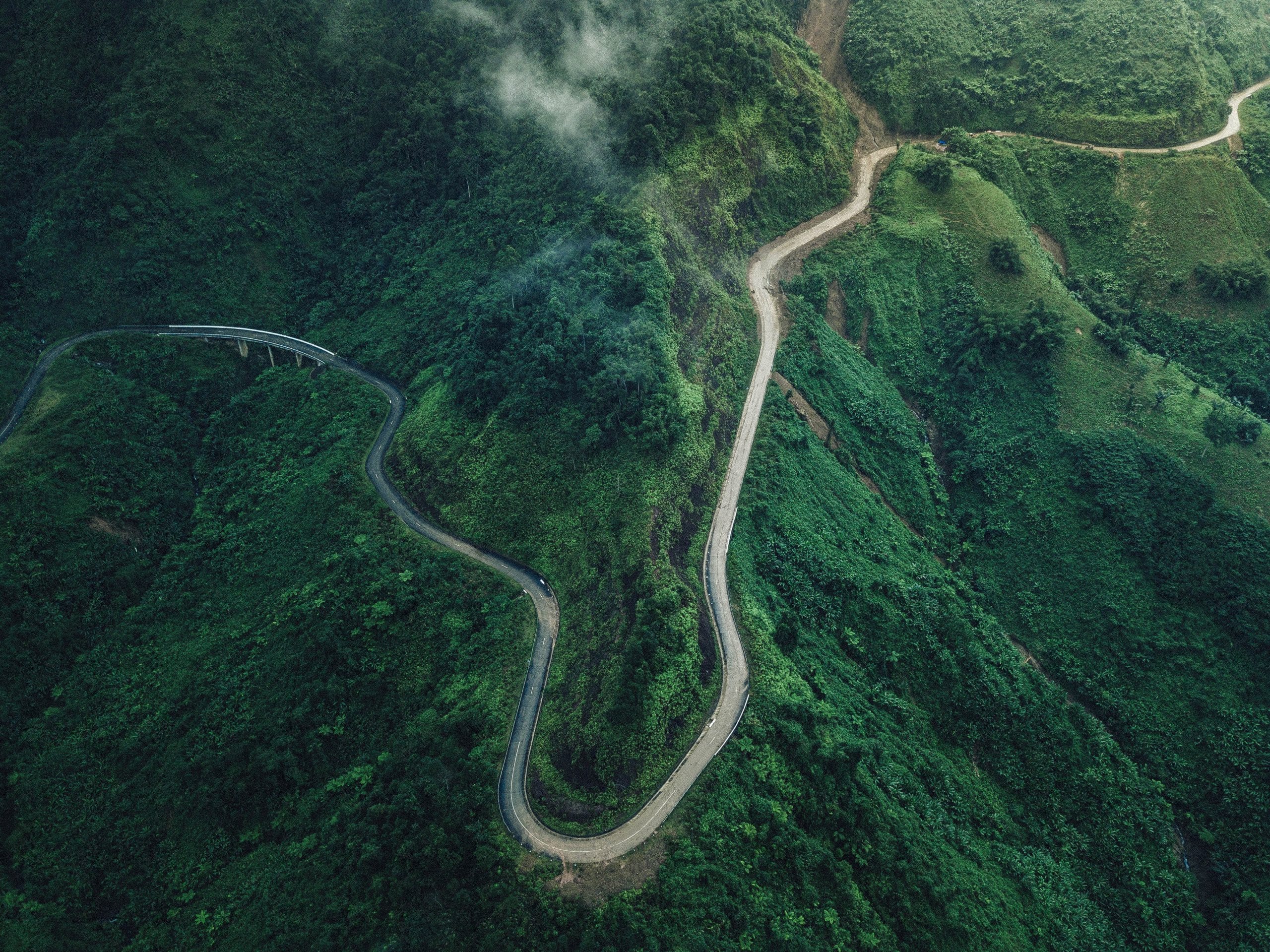 A winding road cuts through lush, green mountainous terrain with clouds hanging low, creating a scenic view reminiscent of the meticulous planning found in the importance of ISO certification.